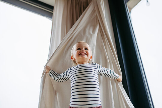 Adorable toddler boy playing hide and seek at home.