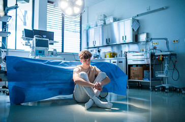 Worried teenage patient sitting alone on hospital floor, struggling with mental health issues.