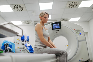 Woman sitting on CT scanner bed, waiting for examination