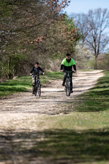Fototapeta premium Father and son enjoy a bike ride on a sunny day, along a dirt path through a wooded area.