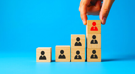 Hand placing a red leader block on top of a wooden block pyramid against a blue background scene