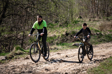 Obraz premium Father and son enjoy a sunny bike ride on a dirt trail through the woods.