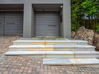 Modern entrance with a minimalist design, with white marble steps to a recessed doorway framed by a gray rectangular structure. A security camera is mounted nearby. Athens, Greece.