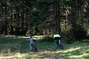 Fototapeta premium Father and son walk bikes through forest trail