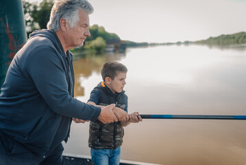 Grandfather helping grandson fishing with rod in river
