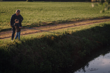 Grandfather teaching grandson how to fish in a countryside river