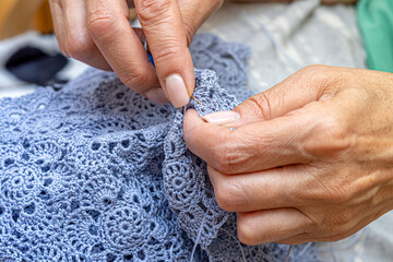 Close up of hands of unrecognizable woman knitting handmade clothes with spokes using  wool yarn....