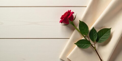 Single red rose on a beige fabric atop a white wooden surface