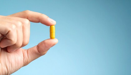 hand holding a yellow pill on light blue background 