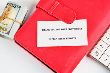 A thank you note is positioned on a vibrant red notebook, next to a stack of cash and a calculator. This arrangement reflects appreciation for continuous improvement endeavors