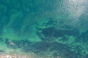aerial perspective of clear ocean with visible underwater rocks, top down aerial drone view