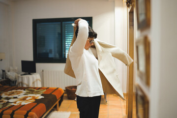 Stylish senior woman is putting on her coat in the hallway of her cozy home, preparing to leave for an appointment or social gathering, embracing independence and active lifestyle