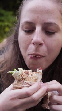 A girl bites into a tasty falafel wrap while standing near a popular food stand in the heart of Sofia