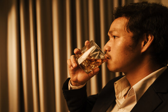 A stylish man holds a glass of whiskey at an upscale bar, enjoying a luxurious indoor celebration with friends and fine alcohol.