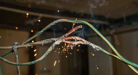 Damaged electrical wires with exposed copper and green ground wire emitting sparks and smoke