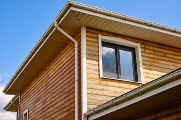 wooden house facade with gutter. modern architectural design showcasing vertical wooden siding and clean roofline under bright blue sky. contemporary eco-friendly home construction