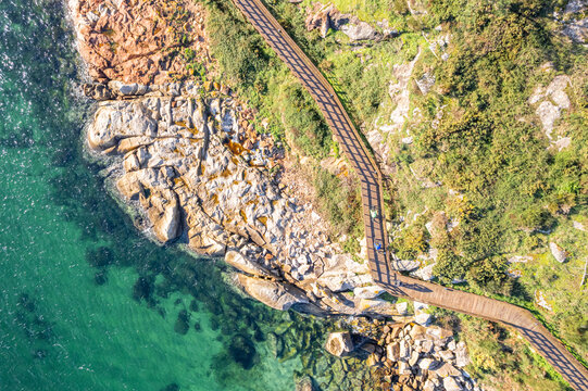 zenithal aerial drone view of two person walking along a wooden walkway on a rocky coast, summer background concept - Powered by Adobe