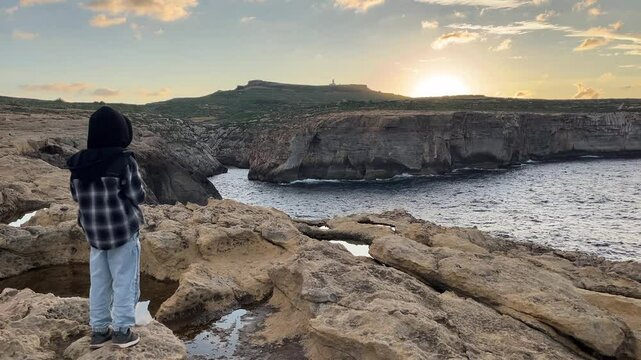 A boy on a rock near the sea. A beautiful sea sunset.