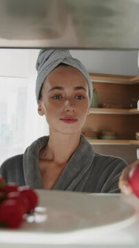 Beautiful caucasian woman in robe opens refrigerator full of healthy food and takes an apple. POV from inside the frige.