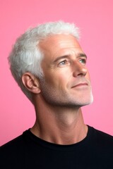 Obraz premium Concept art of style for aging men. A graceful man with a warm and welcoming smile. Pink solid background. Modish men's side part haircut - midlife white man with white hair.