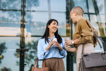 Businesswomen engaging in conversation outside office building while enjoying coffee