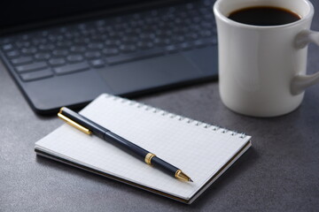 Laptop with cup of coffee and notepad with pen on desk at office
