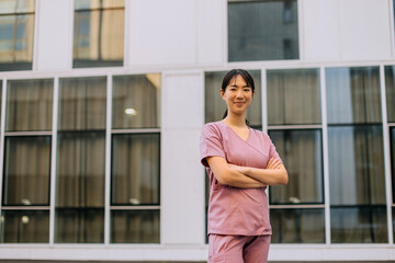 Nurse stands confidently outside a modern hospital building wearing scrubs in a sunny environment