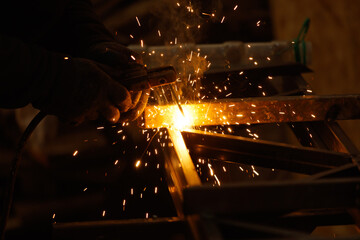 A man is welding a piece of metal, creating sparks and heat