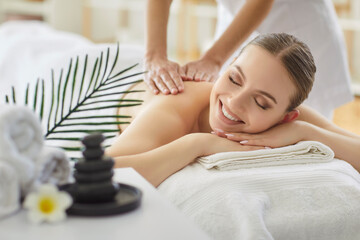Therapist performs back massage for smiling woman in spa salon, providing therapy and body care in...