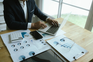 A businesswoman sits at a desk in a corporate office, analyzing financial documents, charts, and...