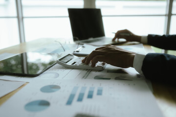A businesswoman sits at a desk in a corporate office, analyzing financial documents, charts, and...