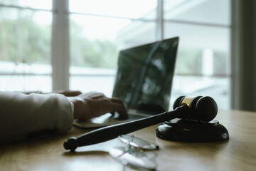 A professional woman lawyer sits at her desk in an office, reviewing legal documents with a gavel and law books nearby.