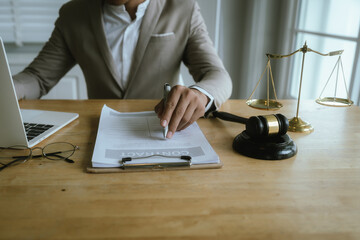 A professional woman lawyer sits at her desk in an office, reviewing legal documents with a gavel and law books nearby.