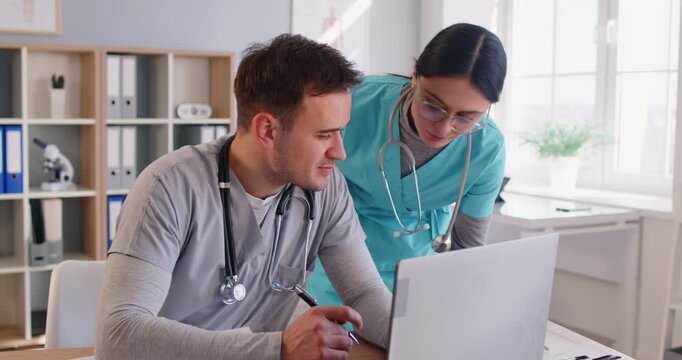 Man doctor and nurse collaborating together, focused at laptop screen, discussing healthcare technology and treatment plan, meeting in clinic office, considering patient case together