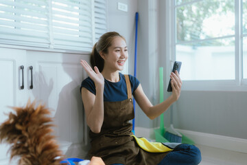 A smiling woman enjoys tidying her cozy, colorful apartment, organizing bookshelves and cleaning...
