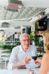 Senior couple toasting wine, enjoying intimate moment during outdoor dining, radiating happiness while sharing romantic lunch on sunny terrace during vacation getaway