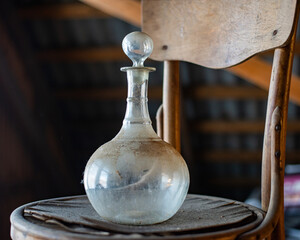 Dusty Vintage Glassware, Clear vintage glass decanter on a seat. Antique room with window
