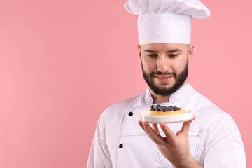 Happy confectioner in uniform holding tart with blueberries on pink background