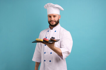 Happy confectioner in uniform holding delicious eclairs on light blue background
