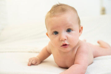 a baby lying on bed in bedroom looking at camera. Adorable naked baby lying on stomach. Happy baby morning.	