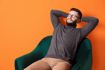 Smiling man relaxing on armchair against orange background