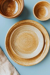Pastel-colored tableware, including a cup, bowl, and plate, is depicted with linens and a wooden spoon in a still life