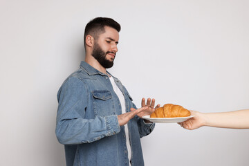 Gluten free diet. Man refusing from croissant on light grey background