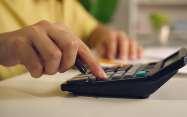 Close up woman hand using calculator to calculate home finance and writing note, accounting on table, budget management. Doing finance, budgeting and tax calculation, monthly expenses