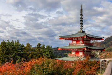 Obraz premium Chureito Pagoda stands among vibrant autumn foliage under a sky filled with textured clouds within Arakurayama Sengen Park creating a peaceful landscape in Japan