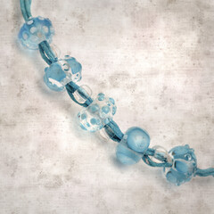 textured stylish old paper background, square, with a simple necklace of blue and transparent glass...