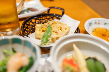 Lotus root and green pepper tempura served in a black basket as part of a traditional Japanese kaiseki dinner with dipping sauce and seasonal dishes