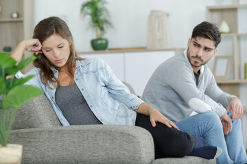 sad woman sits near boyfriend on the sofa