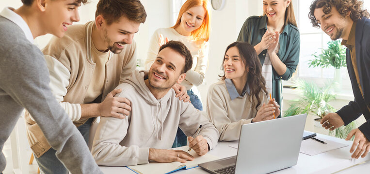 Group of happy college university students celebrating successful launch of digital online project. Team of smiling young adult friends in classroom with laptop computer. Education technology concept