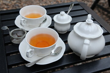 Cups of tea with teapot on a wooden table in a garden
